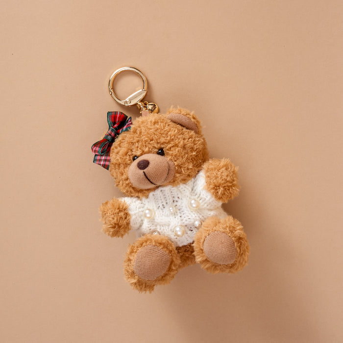 A Pearls & Plaid Teddy Bear Bag Charm by The Darling Effect featuring a plush teddy bear wearing a white sweater embellished with pearls and a plaid bow on its head.