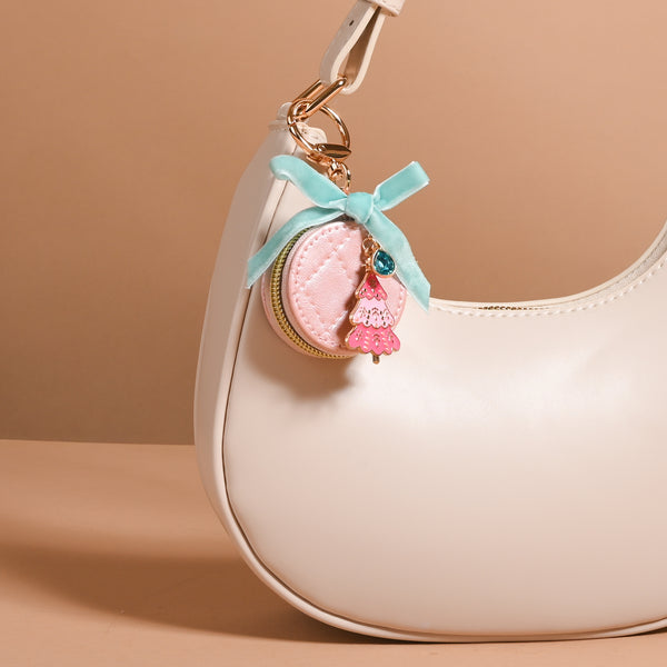 A round, quilted pink Frosted Pink Travel Jewelry Case Bag Charm by The Darling Effect hangs from a handbag, decorated with a light blue ribbon bow and a small pink Christmas tree pendant.