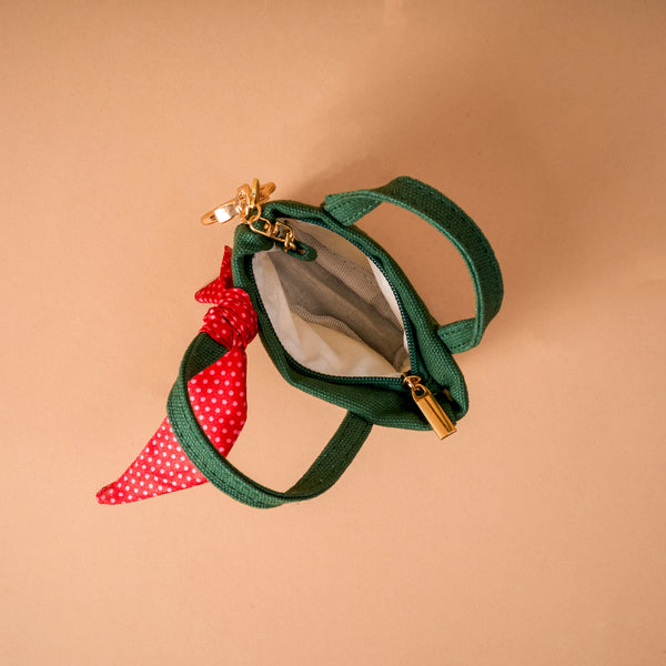 A Merry Little Bow Tiny Tote Bag Charm featuring a miniature forest green canvas tote with a red and white polka dot ribbon tied to the handle.