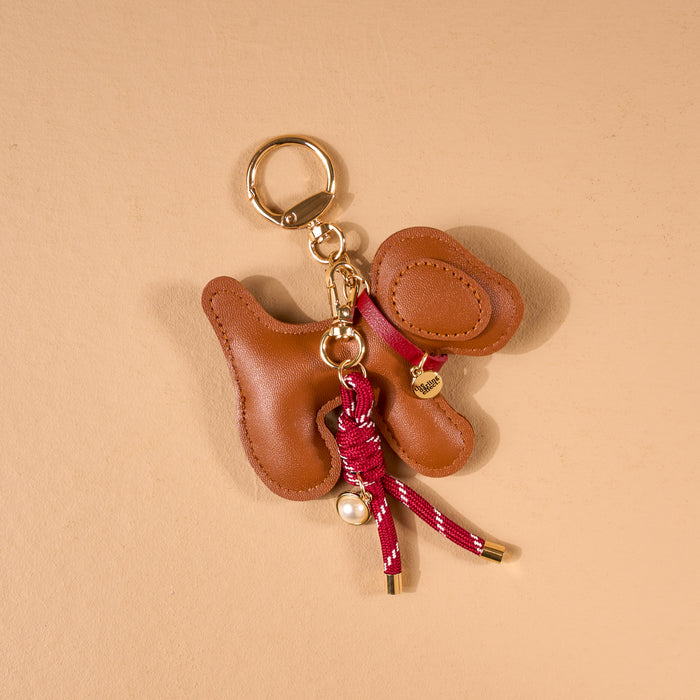 Posh Pup Vegan Leather Bag Charm in brown, shaped like a dog with a red rope leash, gold hardware, and a small pearl bead.