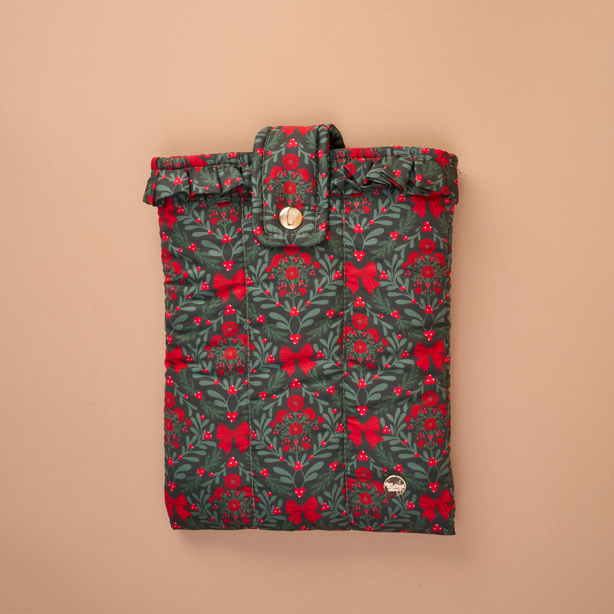 A Merry Moment Book Cover, a quilted sleeve featuring a festive green, red, and white pattern of bows, berries, and pine needles, secured with a ruffled top flap and a snap button for added book protection.