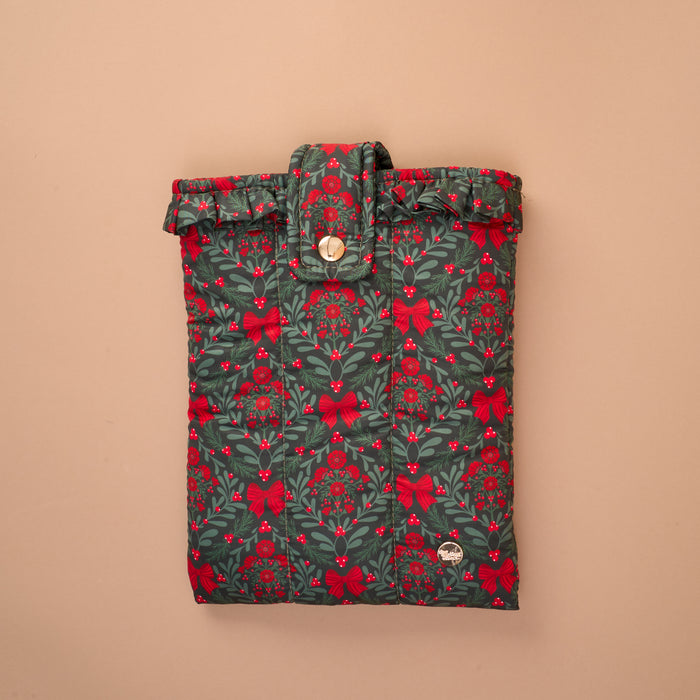A Merry Moment Book Cover, a quilted sleeve featuring a festive green, red, and white pattern of bows, berries, and pine needles, secured with a ruffled top flap and a snap button for added book protection.