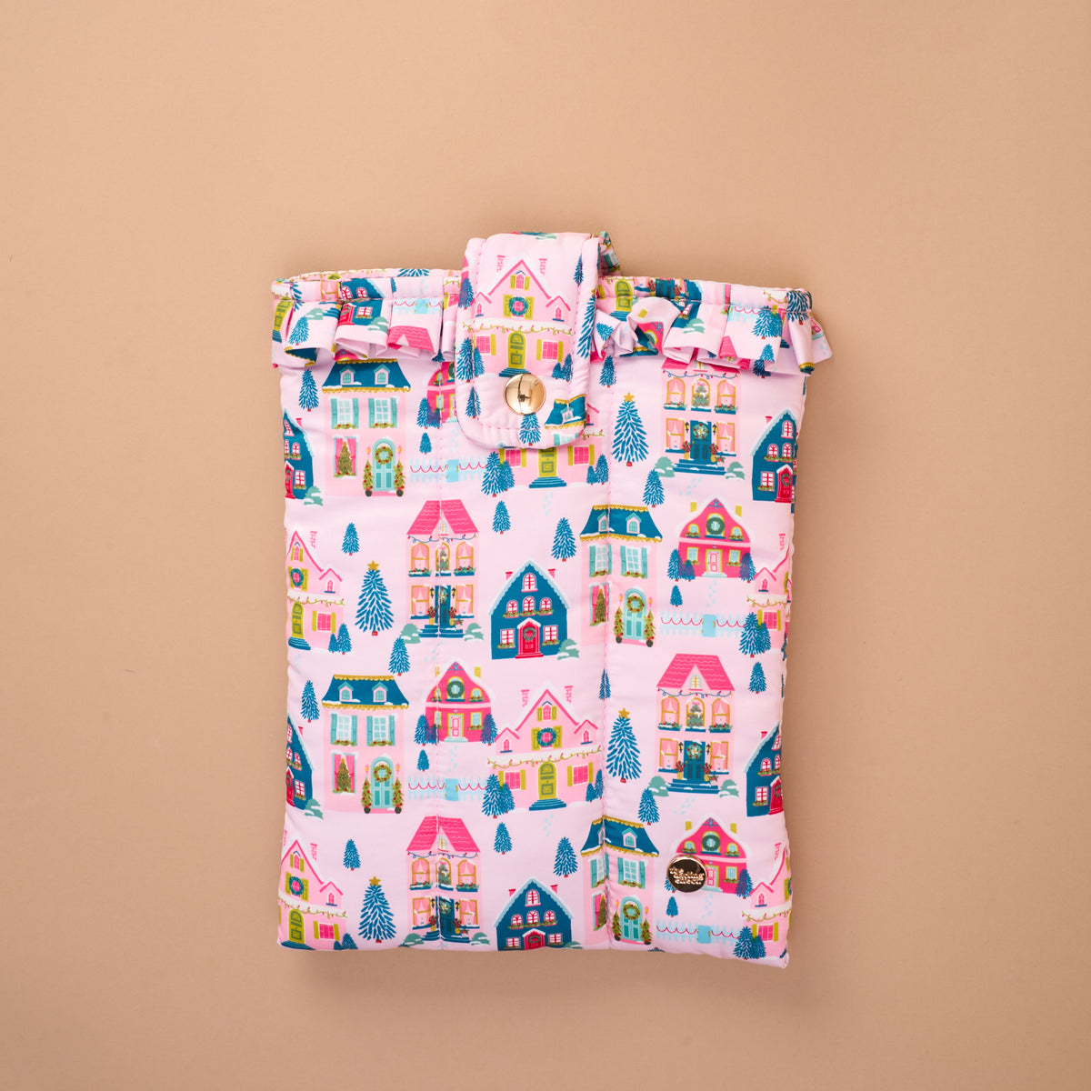A pink quilted Sugarplum Lane Book Cover in a holiday village pattern with houses and Christmas trees, finished with a ruffled top edge and a snap closure for secure book protection.