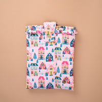 A pink quilted Sugarplum Lane Book Cover in a holiday village pattern with houses and Christmas trees, finished with a ruffled top edge and a snap closure for secure book protection.
