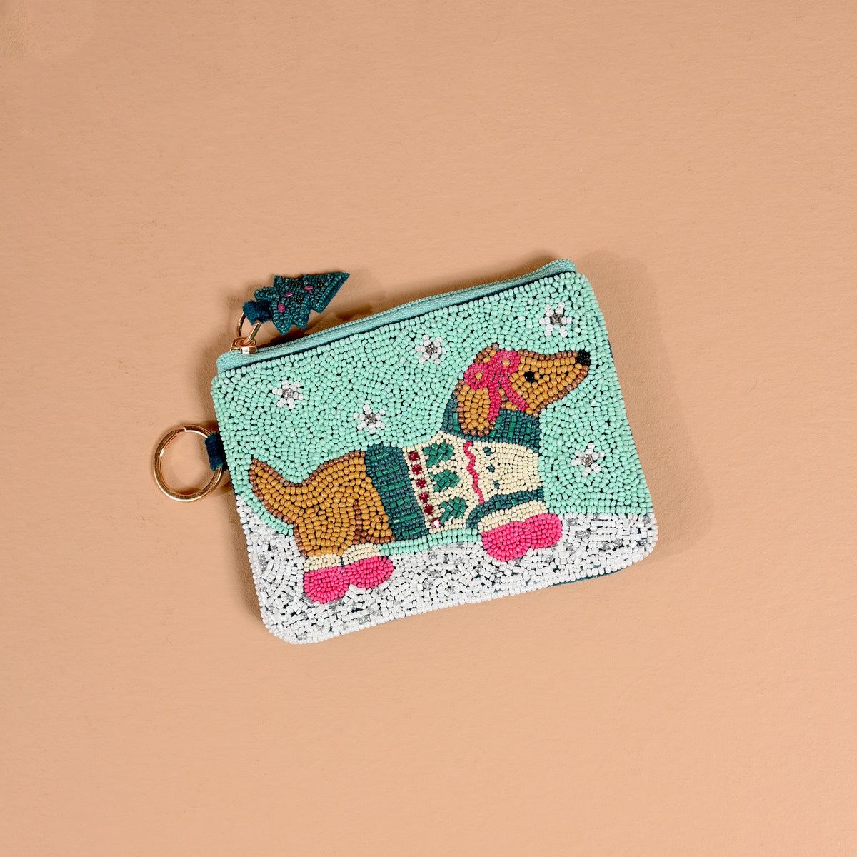The Dashing Dachshund Handcrafted Beaded Pouch is a mint green, handcrafted beaded pouch featuring a dachshund in a patterned sweater and pink boots, with a small Christmas tree charm on the zipper pull.