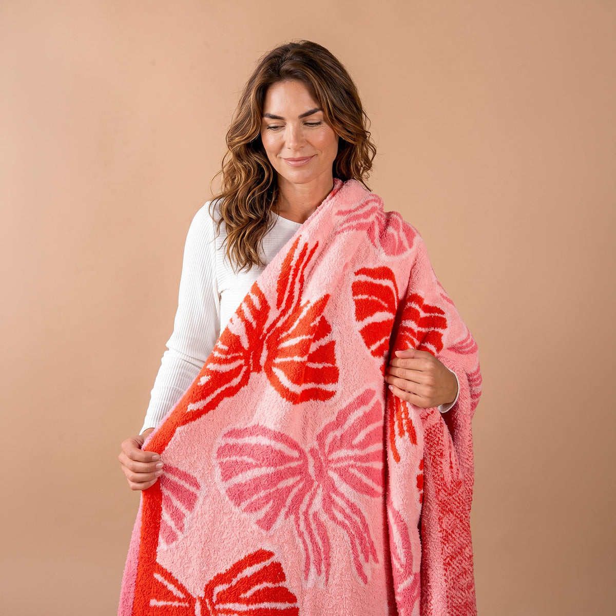 A woman holds up a Wrapped in Bows Cozy Dreams Luxe Blanket featuring a pattern of large pink and red bows.