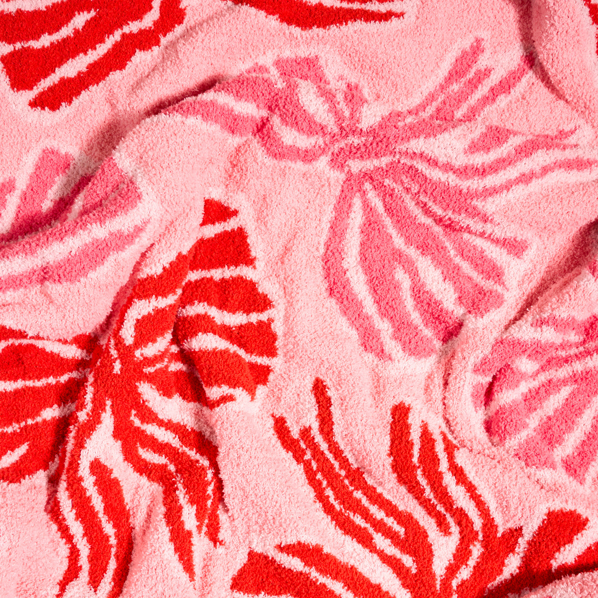 Wrapped in Bows Cozy Dreams Luxe Blanket, an ultra-soft microfiber blanket featuring a repeating pattern of pink and red bows.