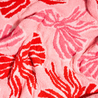 Wrapped in Bows Cozy Dreams Luxe Blanket, an ultra-soft microfiber blanket featuring a repeating pattern of pink and red bows.