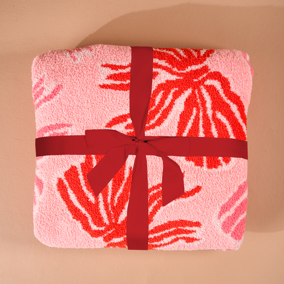 A folded, ultra-soft pink microfiber Wrapped in Bows Cozy Dreams Luxe Blanket by The Darling Effect featuring red leaf-like patterns and tied with a red ribbon.
