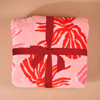 A folded, ultra-soft pink microfiber Wrapped in Bows Cozy Dreams Luxe Blanket by The Darling Effect featuring red leaf-like patterns and tied with a red ribbon.