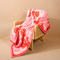 A Wrapped in Bows Cozy Dreams Luxe Blanket with a pink and red bow pattern draped over a wooden chair.