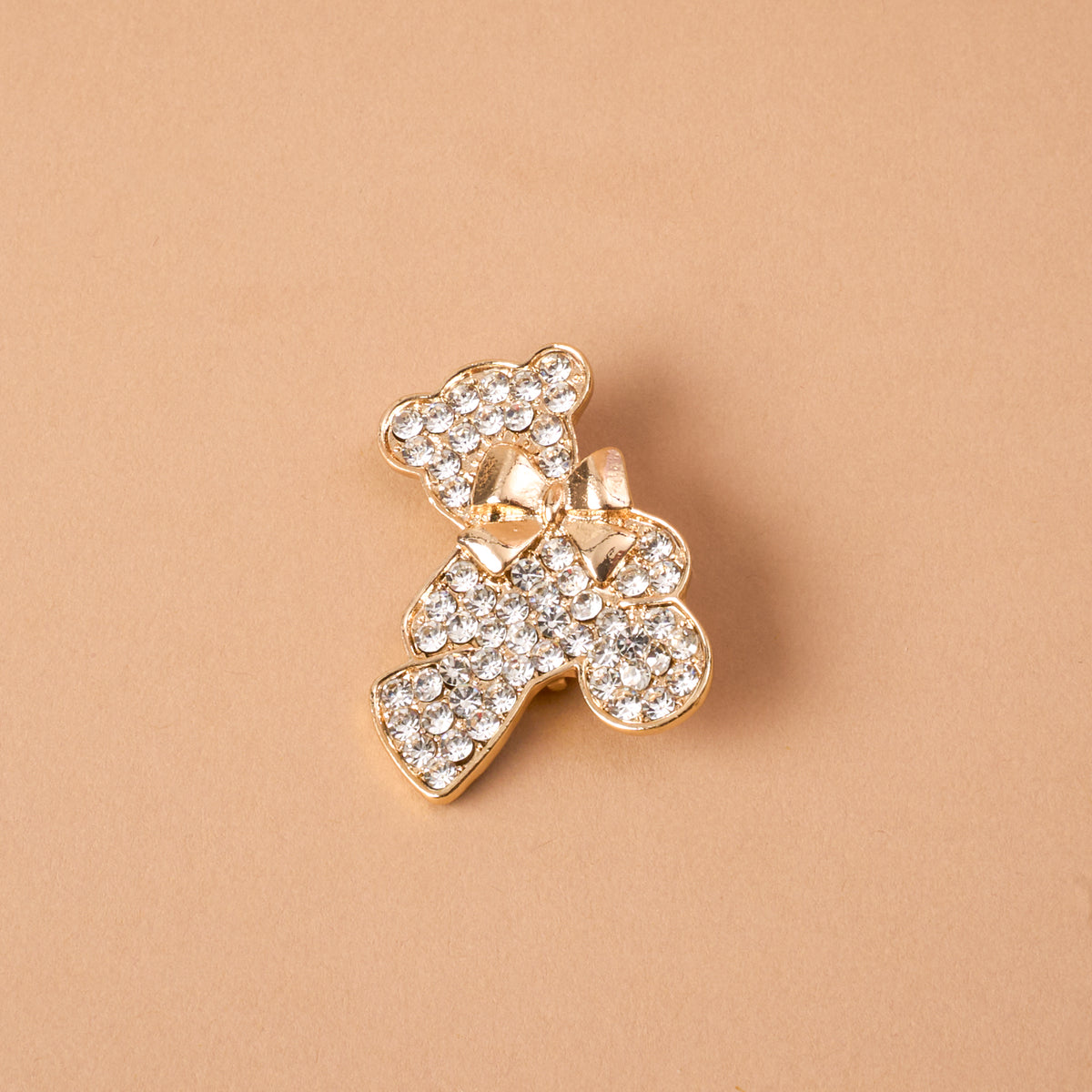 The Crystal Teddy Bear Timeless Brooch by The Darling Effect is a gold-tone teddy bear brooch covered in clear crystals with a small bow at the neck, serving as a vintage-inspired keepsake accessory.