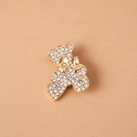 The Crystal Teddy Bear Timeless Brooch by The Darling Effect is a gold-tone teddy bear brooch covered in clear crystals with a small bow at the neck, serving as a vintage-inspired keepsake accessory.