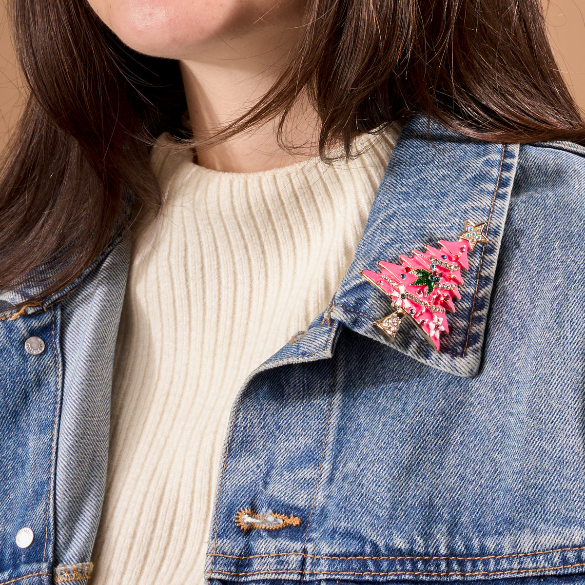 A Whimsical Tree Timeless Brooch, a vintage-inspired pink Christmas tree with colorful accents, pinned to the collar of a denim jacket.