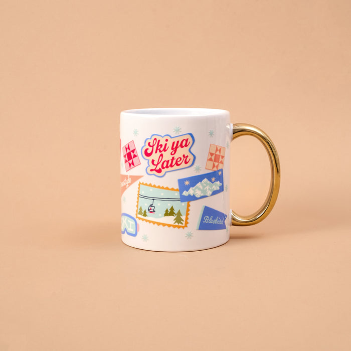 Ski Ya Later 11 oz Cozy Cute Ceramic Mug in white with a gold handle, decorated with ski-themed stickers including a chairlift, snowy mountains, and the text Ski ya Later.
