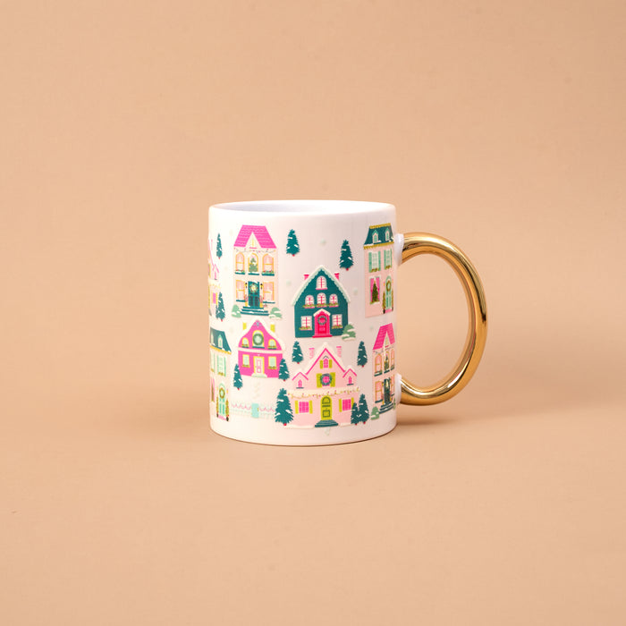 Pink Pine Village 11 oz Cozy Cute Ceramic Mug featuring a white ceramic design with a gold handle and a repeating pattern of colorful, festive holiday houses and pine trees.