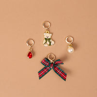 Four gold-tone jewelry charms from the Comfort & Joy The Ultimate Charm Pack, including a teddy bear with a green scarf, a red teardrop gem, a white pearl, and a red and green plaid fabric bow.