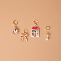 Twinkle Town The Ultimate Charm Pack featuring four gold hoop charms: a pink teardrop gem, a pink bow, a Christmas-themed house, and two small pearls.