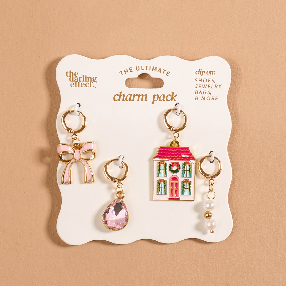 Twinkle Town The Ultimate Charm Pack featuring four decorative accessories: a pink bow, a teardrop-shaped crystal, a two-story house with a festive wreath, and a cluster of pearls, displayed on cardboard backing.
