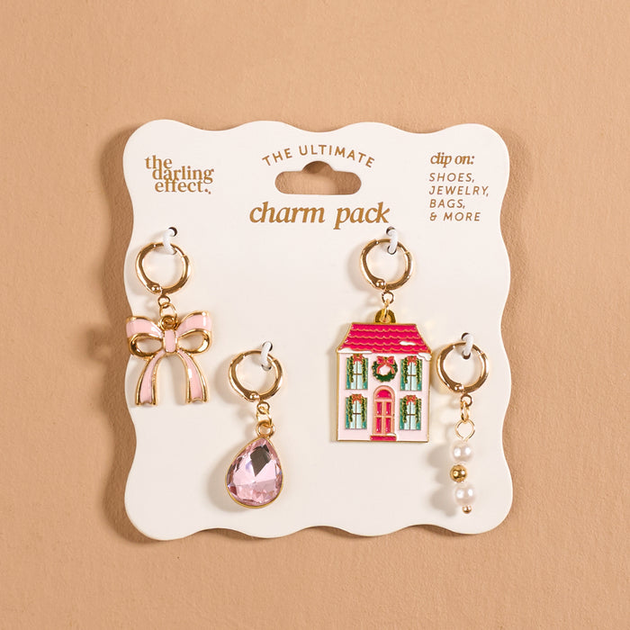 Twinkle Town The Ultimate Charm Pack featuring four decorative accessories: a pink bow, a teardrop-shaped crystal, a two-story house with a festive wreath, and a cluster of pearls, displayed on cardboard backing.
