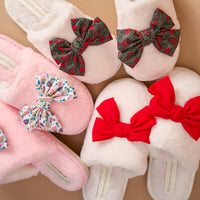 Three pairs of Betty Bow Red On Cloud Nine Slippers by The Darling Effect, featuring large bows in red, festive floral, and winter village patterns.