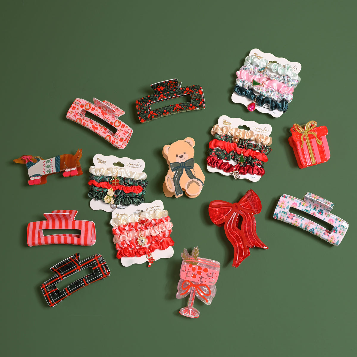 A collection of hair accessories including an Evergreen Plaid Claw Clip, various other printed claw clips, colorful hair scrunchies on cards, and clips shaped like a dachshund, a teddy bear, a gift box, and a stemmed cocktail glass.