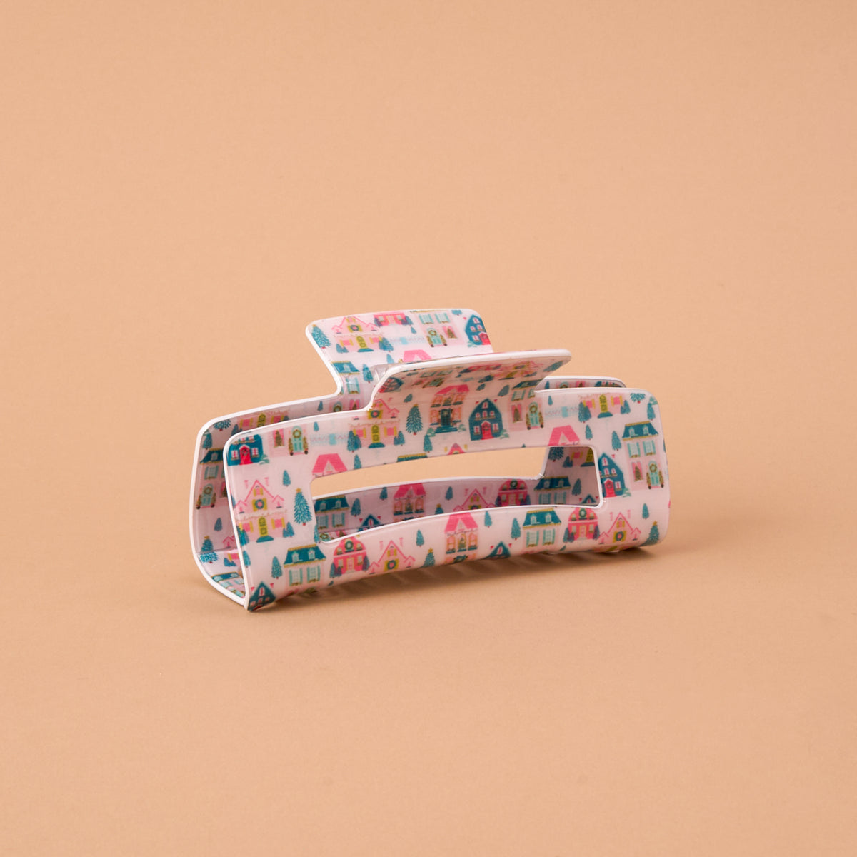 Sugarplum Lane Claw Clip in a rectangular, light pink design featuring a pattern of colorful houses and evergreen trees.