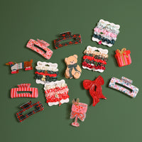 A collection of hair accessories including a Sugarplum Lane Claw Clip, various holiday-themed scrunchie sets, and decorative hair pins arranged on a green background.