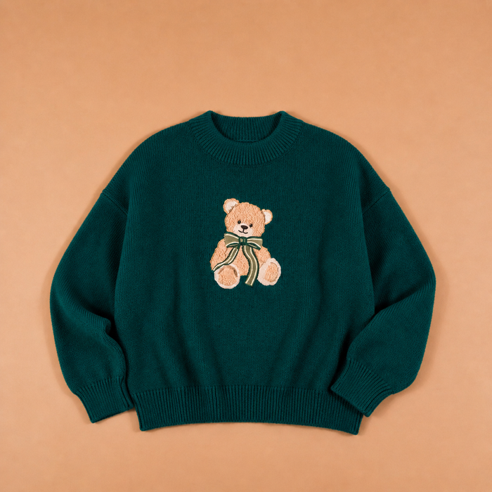 Teddy Bear Theo Classic Sweater by The Darling Effect, a dark green crewneck holiday sweater featuring an embroidered teddy bear wearing a striped bow.