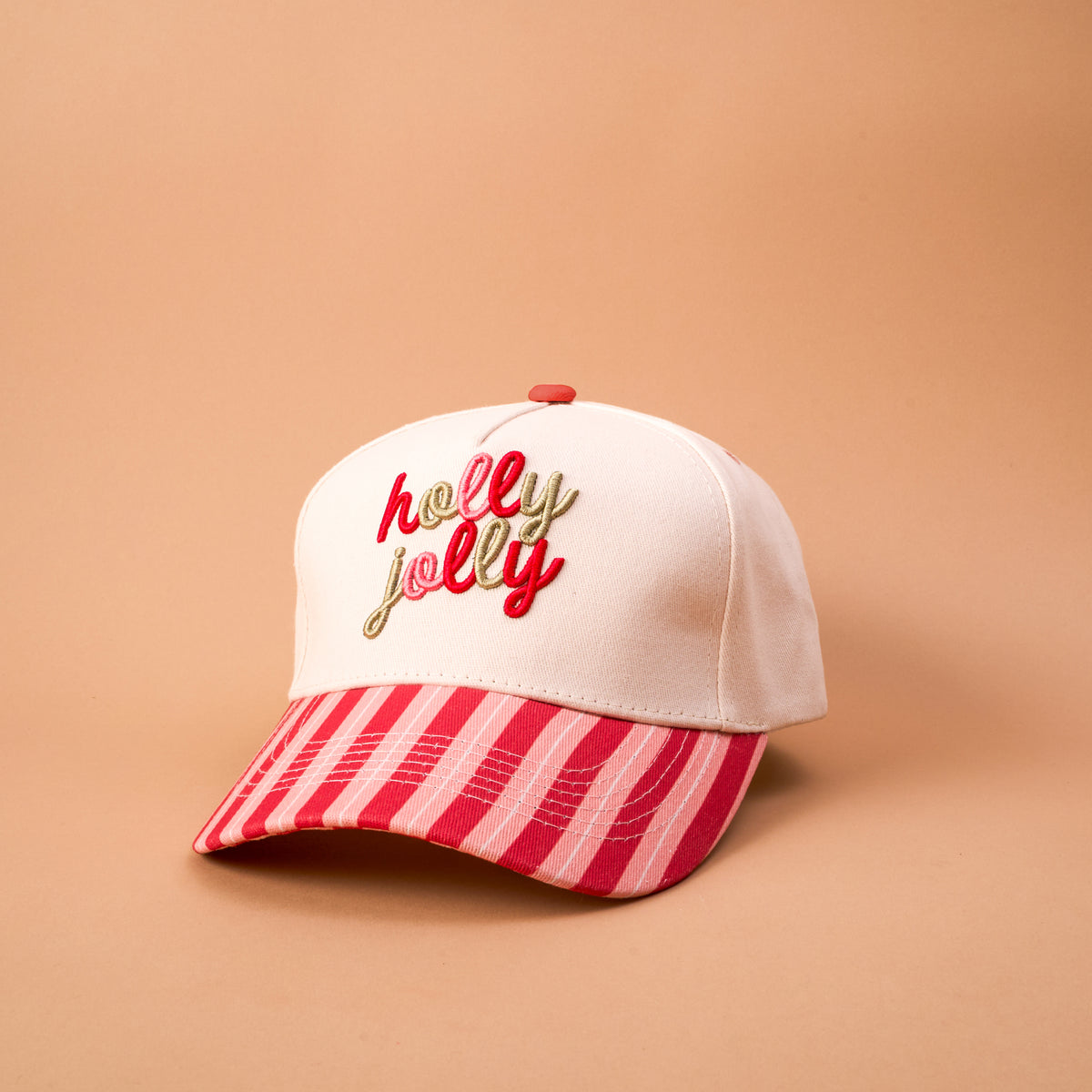 A Holly Jolly Classic Canvas Hat by The Darling Effect featuring a light pink crown, a red and pink striped brim, and holly jolly embroidered in red and gold on the front.
