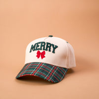 The Darling Effect Merry Classic Canvas Hat is a beige baseball cap with a green plaid brim, embroidered with the word MERRY in dark green letters above a small red bow.