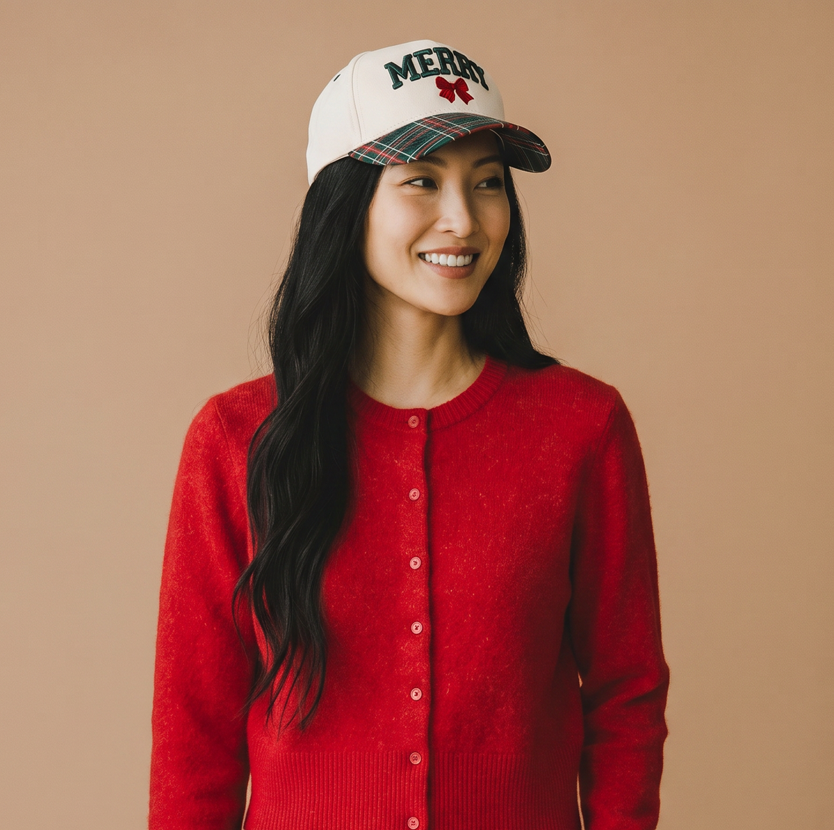 A smiling woman wearing The Darling Effect Merry Classic Canvas Hat, a cream-colored cap with green embroidered text and a plaid brim.