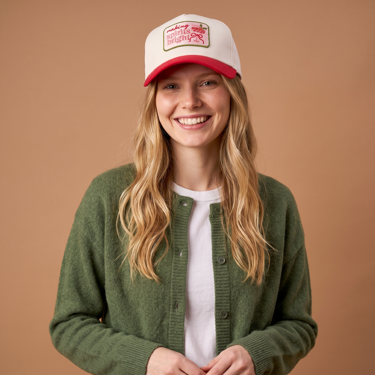 A smiling woman wears a white and red Making Spirits Bright Classic Canvas Hat featuring a patch that says making spirits bright with a red bow graphic.