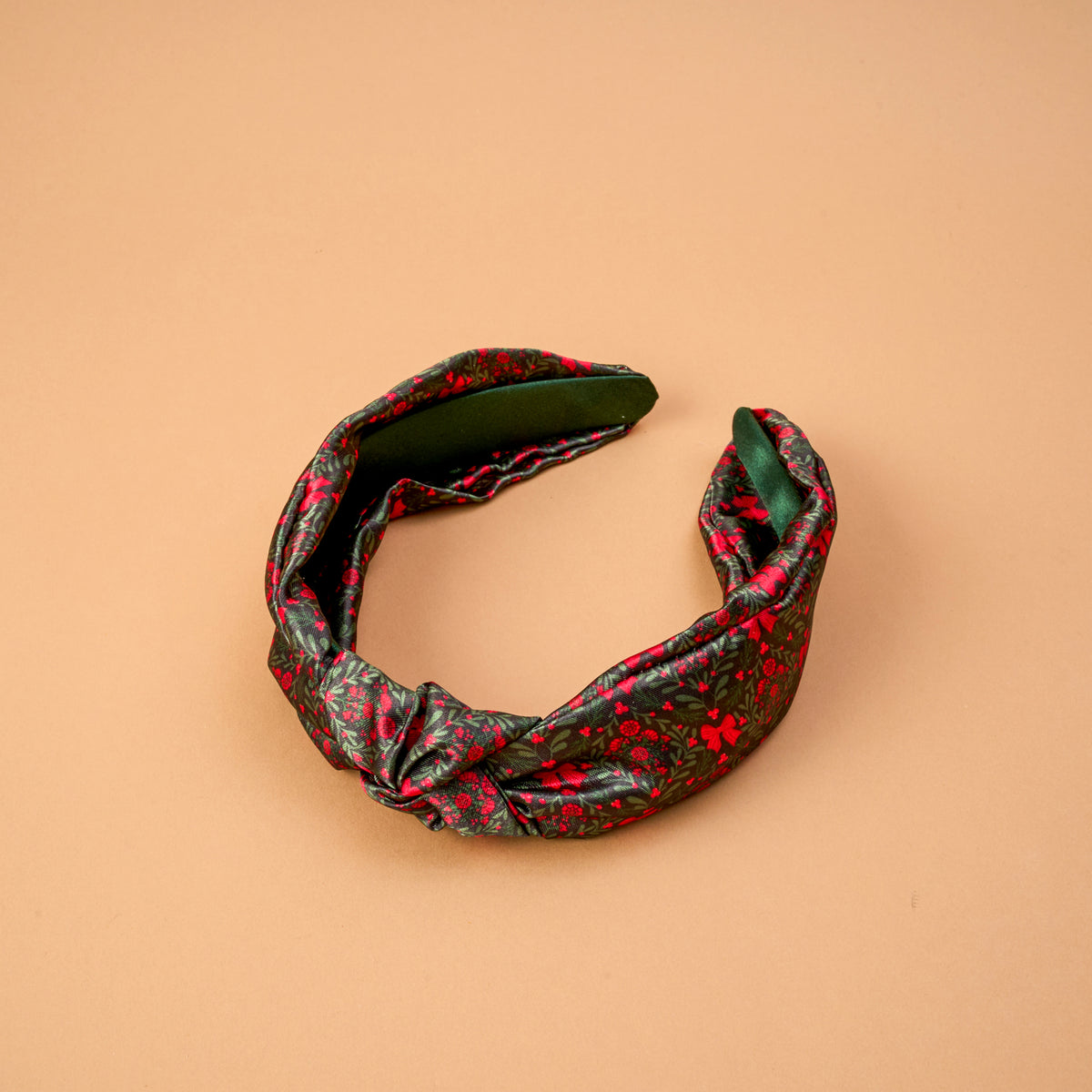 A Merry Moment Classic Twist Headband featuring a green and red floral pattern, a dark green interior lining, and a twist detail.