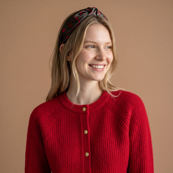 A woman wears The Darling Effect A Merry Moment Classic Twist Headband, featuring a dark patterned knotted twist design.