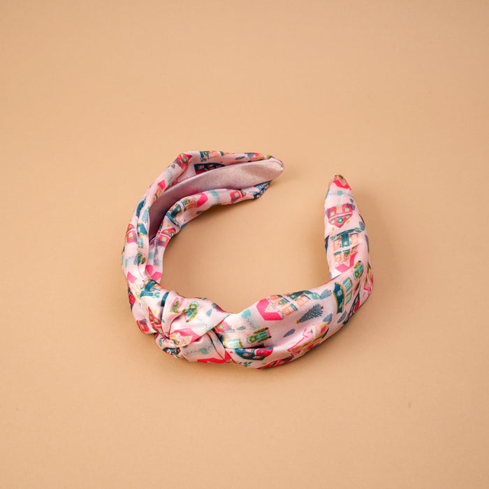 Sugarplum Lane Classic Twist Headband in pink fabric featuring a whimsical print of small houses and trees.