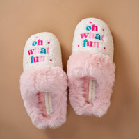 Cream-colored Oh What Fun Dreamy Daze slippers featuring pink faux-fur trim and the embroidered text oh what fun on the top.