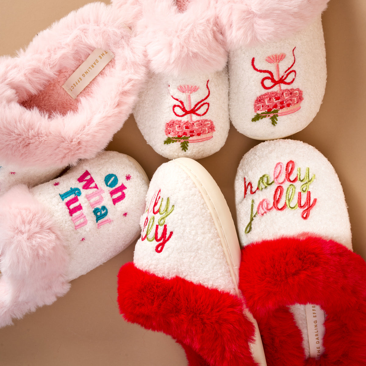 Three Oh What Fun Dreamy Daze Slippers with faux-fur collars: one pair with red and green holly jolly text, and a single slipper with pink and blue oh what fun text and a tiered cake graphic.