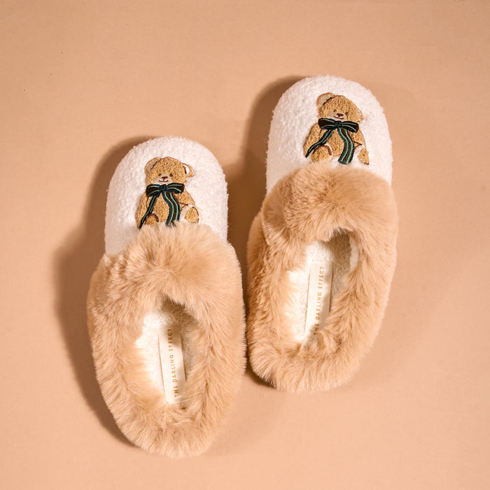 Pair of cream-colored Teddy Bear Theo Dreamy Daze Slippers by The Darling Effect, each featuring an embroidered teddy bear wearing a green ribbon and a cozy faux-fur collar.