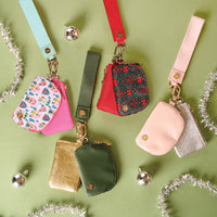 Four Rosé All Day Dynamic Duo Pouch Luxe Wristlets with matching straps, each featuring two zippered compartments in various colors, patterns, and textures, arranged on a green background with decorative silver accents.