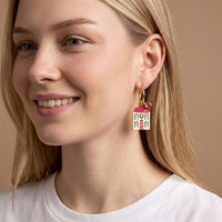 A woman wearing BowBelle Manor Signature Hoop Earrings, gold charms shaped like a two-story house with a pink roof.
