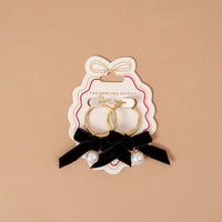 Midnight Velvet Signature Hoop Earrings featuring lightweight gold hoops on a display card, each decorated with a black ribbon bow and a hanging white pearl bead.