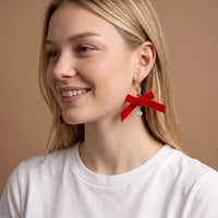 Ruby Ribbon Signature Hoop Earrings featuring a red ribbon bow and a small dangling crystal charm worn on a person.