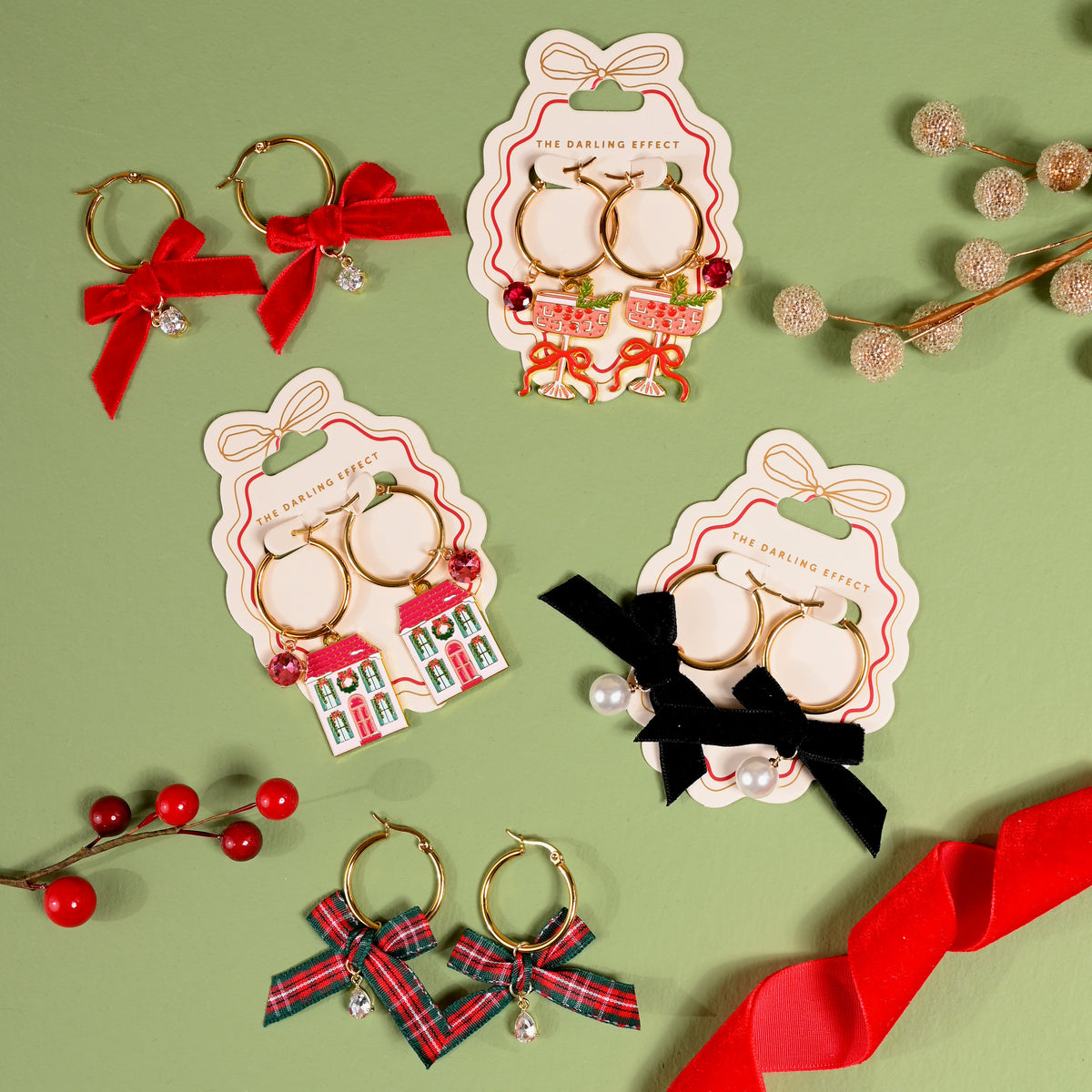 Five pairs of Ruby Ribbon Signature Hoop Earrings by The Darling Effect on display cards, featuring holiday accents including red bows, cocktail glasses, houses, black bows with pearls, and plaid bows.