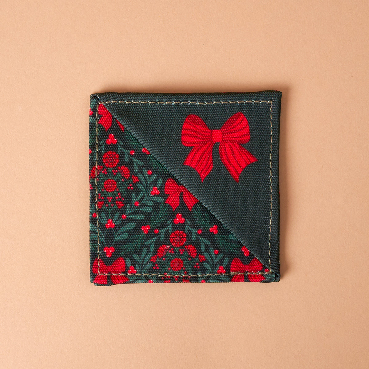 A Merry Moment Corner Keeper fabric bookmark, shaped as a triangle with dark green holly leaves and red berries on one side and a solid dark green section with a red bow print on the other.
