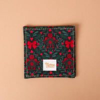 A Merry Moment Corner Keeper fabric bookmark featuring a pattern of red bows, berries, and green holly leaves, with a The Darling Effect brand tag centered at the bottom.