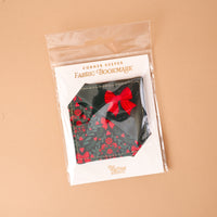 A Merry Moment Corner Keeper Fabric Bookmark with a triangular holiday floral pattern and a red fabric bow, packaged in a clear plastic sleeve on a branded card.