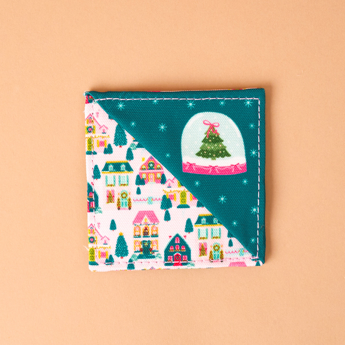 Sugarplum Lane Corner Keeper Fabric Bookmark with a diagonal divide, featuring a snowy village scene on one side and a teal background with a Christmas tree snow globe on the other.