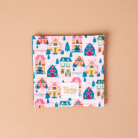 Sugarplum Lane Corner Keeper Fabric Bookmark featuring a repeating pattern of colorful houses and trees on a light pink background, with a The Darling Effect brand label sewn in the bottom corner; a perfect book lover gift.