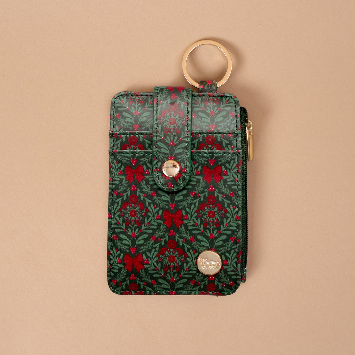 A Merry Moment Keychain Wallet in festive green and red, featuring a gold key ring and a holiday pattern of bows, holly, and sprigs.